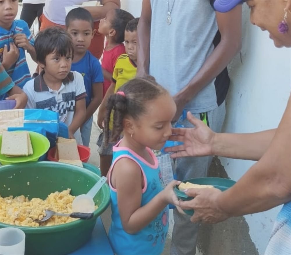 Niña recibiendo alimento de manos de una voluntaria durante una jornada comunitaria