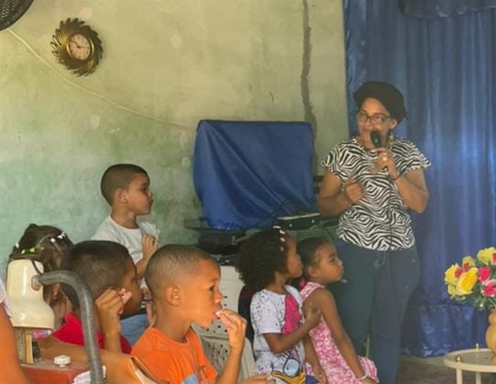 Niñas y niños en un taller de capacitación con máquinas de coser junto a una lideresa comunitaria